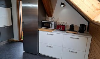 A modern kitchen with a stainless steel refrigerator, microwave, and a kettle. The wooden paneling and the window create a bright and inviting atmosphere.