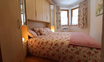 A cozy bedroom with a large bed and floral bedding. The windows are adorned with curtains, and there is warm light from bedside lamps.