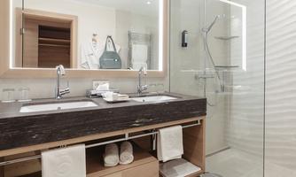 A modern bathroom with double sinks and large mirrors. The shower is enclosed in glass and the space is bright and inviting.