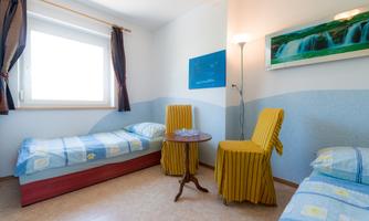 A simple room with two beds and a small table. The walls are painted in soft colors, and a window lets in plenty of light.