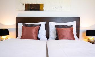A cozy bedroom with two single beds and elegant pillows. Soft lighting from bedside lamps creates an inviting atmosphere.