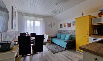 A bright kitchen with a dining area and a cozy seating corner. The walls are decorated and a yellow kitchen unit provides a cheerful accent.