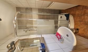 A small bathroom with a modern shower and a sink. The walls are tiled, and the decor is simple and functional.