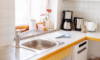 A bright kitchen with a sink and various kitchen appliances. On the countertop, there are flowers and some kitchen utensils.