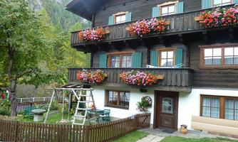 A charming two-story wooden house with colorful flower balconies. The well-maintained garden with a seating area and a ladder creates an inviting atmosphere.