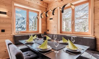 A modern dining room with wooden walls and large windows. The table is beautifully set and offers a view of the snowy landscape.