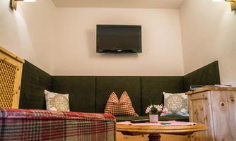 A cozy room with a seating area, decorated with cushions and a wooden tray. A television hangs on the wall, and the room exudes an inviting atmosphere.