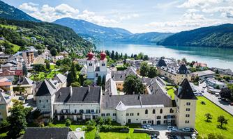 A picturesque town on the shore of a lake, surrounded by mountains. Historic buildings and green spaces shape the landscape.