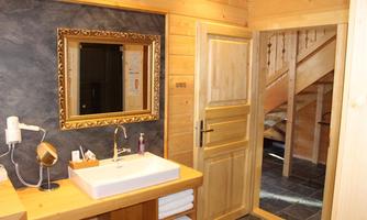 A modern bathroom with wooden paneling and a large mirror. In the background, access to a staircase is visible.