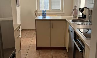 A modern kitchen with bright furniture and tiled flooring. Daylight comes in from a window.
