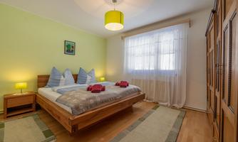 A cozy bedroom with a double bed and blue pillows. The walls are painted green and the light is warm and inviting.