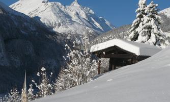 An idyllic winter landscape with snow-covered mountains and a small wooden house. The clear blue sky complements the tranquil scene.