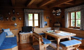 A cozy wooden room with a dining area and a blue seating corner. Bright windows bring a lot of light into the room.