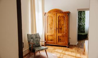 A bright room with a cozy armchair and a classic wooden wardrobe. Large windows provide plenty of daylight.