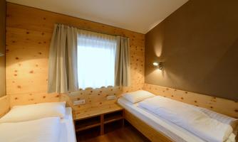 A cozy room with two single beds and wood paneling. The window lets in natural light and creates a friendly atmosphere.