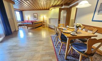 A spacious living area with a wooden ceiling and cozy furnishings. The dining area is decorated with a table, chairs, and a vase of flowers.