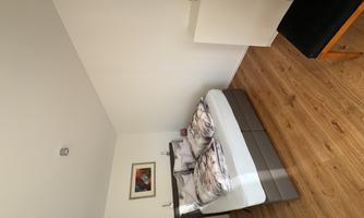 A cozy bedroom with a double bed and modern design. The floor is made of wood, and there is a chair as well as a wardrobe in the room.