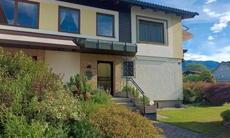 A beautifully designed garden in front of a house with colorful flowers and shrubs. A sunshade protects the entrance area.
