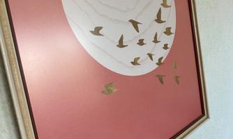 A modern piece of art featuring a large, round motif and several small birds on a delicate pink background. The frame is simple and elegant.
