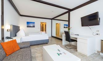 A modern hotel room with a cozy sofa and a bed. There is a desk, a TV, and large mirrors that expand the space.
