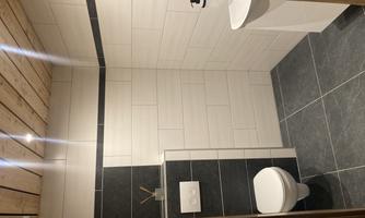 A modern bathroom with bright tiles and dark flooring. There is a toilet and a sink on the wall.