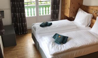 A cozy room with two single beds and wooden paneling. In front of the window overlooking a balcony, the curtains are drawn open.