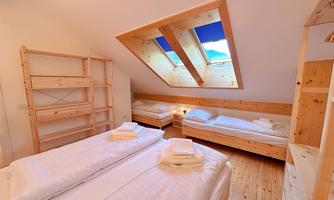 A cozy bedroom with two beds and an additional single bed.  
Large windows provide plenty of light and a view of the sky.