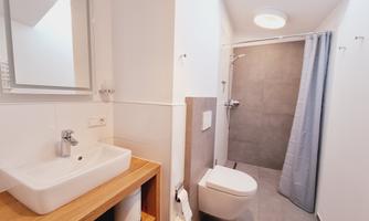 A modern bathroom with a shower, a sink, and a stylish wooden shelf. The walls are light, and the decor is simple and functional.