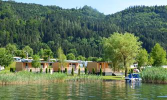 A calm lake with modern holiday homes on the shore. Surrounded by green mountains and trees, it offers a relaxed atmosphere.