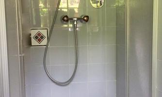 A simple shower cubicle with gray tiles and a showerhead. The walls are decorated with patterned tiles.