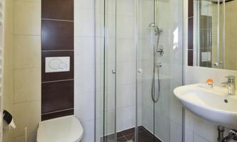 A modern bathroom with a glass shower and a sink. The walls are brightly tiled, and the floor is dark.