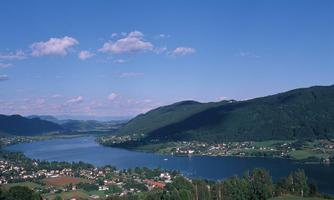 A picturesque landscape with a tranquil lake and surrounding hills. The clouds in the blue sky give the scene a peaceful atmosphere.