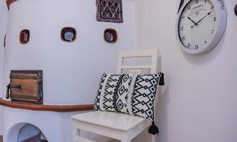 A cozy room with a stove and a bright clock on the wall. On the white chair lies a decorative pillow in black and white.