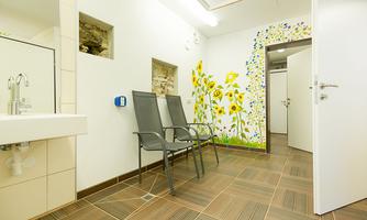A bright room with two chairs and a colorful mural of sunflowers. The floor is tiled with brown tiles and there is a sink.