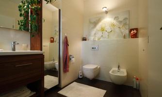 A modern bathroom with a stylish decor. There is a large mirror, a plant decoration, and a beautiful flower print on the wall.