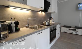 Modern kitchen with white cabinets and gray countertops. Equipped with cooking appliances, sink, and a television.