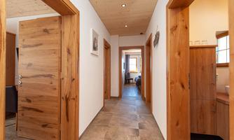 A bright hallway with wooden frames and modern doors. At the end of the hallway, a cozy room is visible.