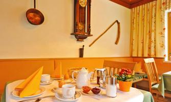 A cozy breakfast table with various treats and a coffee pot. In the background, traditional decorative elements and a wall clock can be seen.