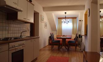 A cozy apartment with a modern kitchen area and a dining space. The room has bright walls and a warm hardwood floor.