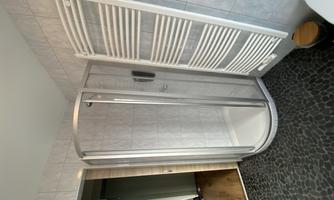 A modern shower in a bathroom with light gray tiles. Next to the shower, there is a towel holder and a small trash bin.