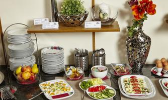 An attractively arranged buffet with various salads and fresh fruit. Beneath it are plates, cutlery, and a decorative vase with flowers.