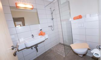 A modern bathroom with a glass shower and a sink. Orange towels add a cheerful touch to the space.