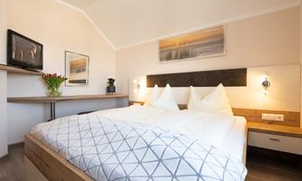 A cozy bedroom with a double bed and modern furniture. A picture hangs on the wall and there is a TV as well as flowers on the table.