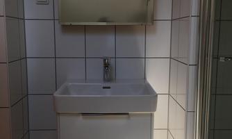A modern bathroom with a white sink and a large mirror. The light shines through a window and illuminates the room.