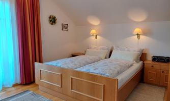 A cozy bedroom with two beds and warm colors. The windows are adorned with curtains, and there is soft lighting on the walls.