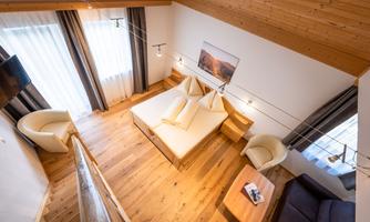 A modern room with wooden flooring and simple furniture. Large windows provide plenty of daylight and a cozy atmosphere.