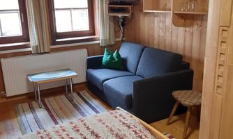 A cozy room with wooden walls, a gray sofa, and a table. The windows provide plenty of daylight and offer a view outside.