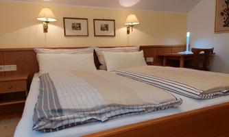 A cozy bedroom with two beds, beautiful bedding, and warm lamps. There is a small table, and the walls are decorated with pictures.
