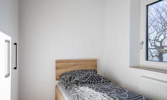 A simple bedroom with a bed and a window. The walls are white and the bedding has a modern pattern.