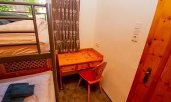 A small room with a bunk bed and a desk. The walls are light, and there is a view outside through the window.